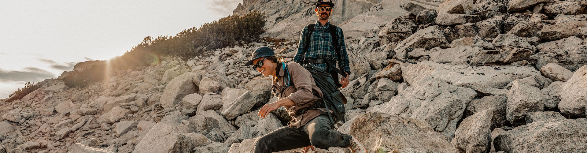 Two people hiking on a rocky mountain trail with a scenic background