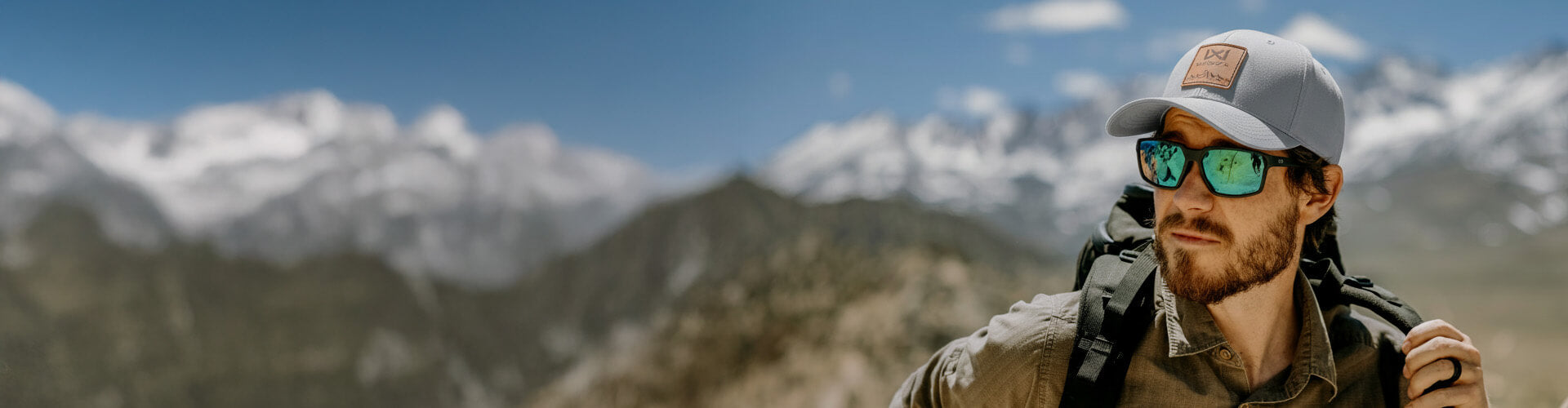Man with sunglasses and cap standing in front of mountainous landscape