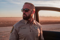 Man in a police uniform standing next to a car in a desert setting
