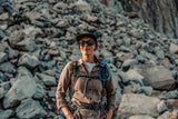 Person standing in front of a rocky background wearing outdoor gear.