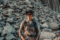 Person standing in front of a rocky background wearing outdoor gear.
